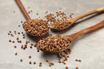 Spoons with dry buckwheat on grey table, closeup
