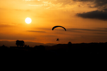 Fototapeta na wymiar Paramotor trike silhouette with the sunset as a background in an orange Summer hot evening