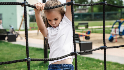 Little girl rides on a swing in an outdoor playground. Children play in the courtyard of a school or kindergarten. Healthy summer fun for kids.