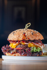 Burger with a cutlet of marbled beef with cheddar cheese, slices of bacon, tomato and pickle in a...