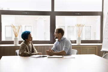 Two positive diverse office friends discussing work business process, teamwork, cooperation,...