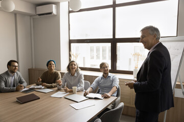 Cheerful elder business leader motivating team for work, inspiring employees in group meeting in...