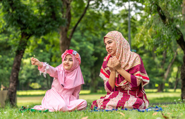 Portrait of happy religious happy love asian islam family muslim mother teaching muslim girls child pray to god with hijab dress, Hari Raya day, Eid al-Fitr, fasting, islam, ramadan in summer park