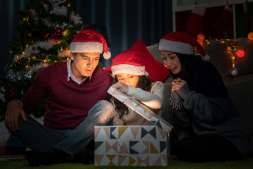 Portrait of happy family father and mother with daughter in santa hats having fun opening magic christmas gift box and enjoying spending time together in christmas time at home