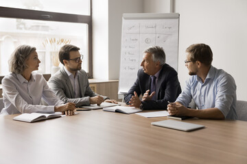 Serious older businessman speaking to business partners, discussing cooperation, partnership, problem solving, negotiating in office boardroom. Boss talking to employees on meeting - obrazy, fototapety, plakaty
