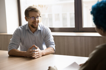 Positive business professional candidate man talking to recruit manager on job interview, discussing resume, smiling. Couple of colleagues, project partners meeting at table, planning strategy