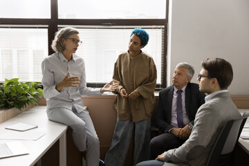 Senior project leader woman speaking to multiethnic creative team, giving instructions, tasks,...