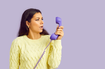 Young long haired woman fearfully holding receiver of landline phone after unpleasant call from bank or leasing company is stressed and depressed because of bad news standing in lilac studio