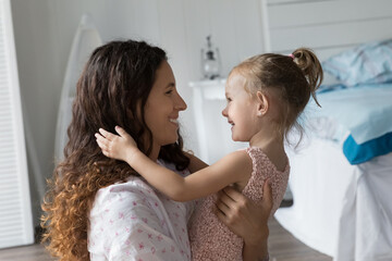 Pretty mother and little daughter sit on floor looks at each other with love. Young mom tenderly...