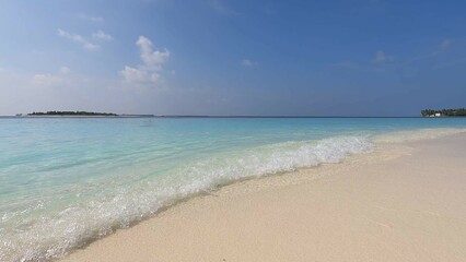 Maldives beach, waves wash the shore with white sand, clear azure water, and blue sky. Beauty, paradise, Indian ocean view