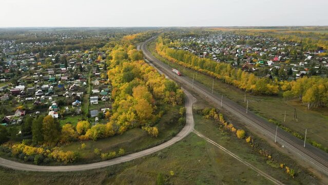 Aerial view of railway traffic running through the countryside and village in autumn day.