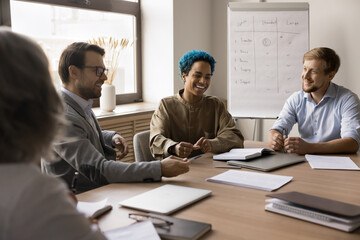 Happy multiethnic business colleagues meeting at large table in boardroom, cooperating on project tasks, working on corporate education together, discussing funny ideas, brainstorming