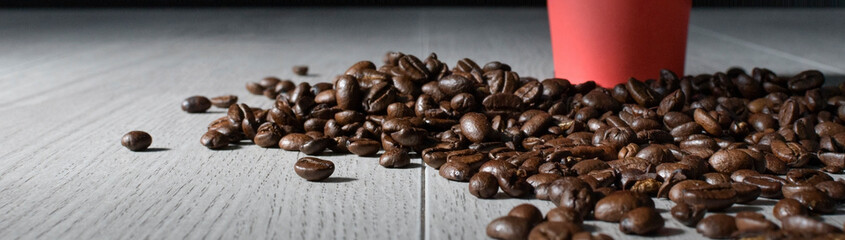 Scattered coffee beans on a beige table and a red mug. Copy space, wide banner