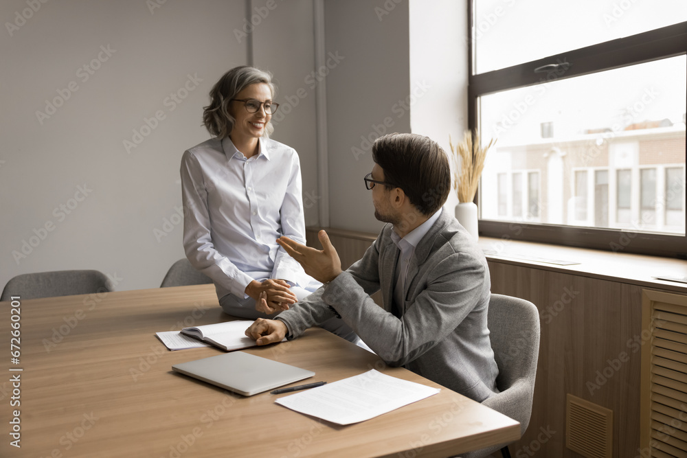 Canvas Prints Two positive project managers discussing project ideas, brainstorming at meeting table, talking, smiling, laughing. Elder professional woman giving advice to younger colleague