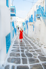 Fototapeta na wymiar Woman in red dress at the Streets of old town Mykonos during a vacation in Greece, Little Venice Mykonos Greece
