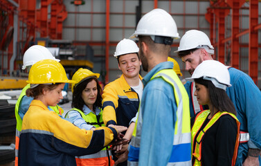 Group of factory workers in hardhats with joint hands together for celebrating success