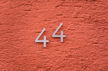 Zahl 44 als Hausnummer an orangefarbener Wand mit Rauputz