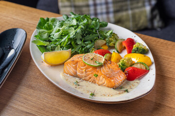 One piece of baked salmon grilled pepper lemon and salt on a brown plate with lettuce leaves. wood background