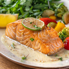 One piece of baked salmon grilled pepper lemon and salt on a brown plate with lettuce leaves. wood background
