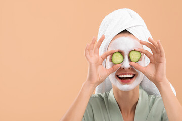 Woman with face mask and cucumber slices on beige background,space for text. Spa treatments
