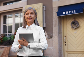 Happy business owner with tablet near her hotel outdoors, space for text