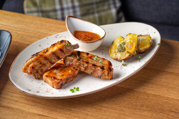 grilled pork ribs served with roast new potatoes on a white plate on a wooden table