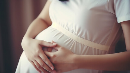 Pregnant woman in dress holds hands on belly on a white background. Pregnancy, maternity, preparation and expectation concept. Close-up, copy space, indoors. Beautiful tender mood photo of pregnancy.