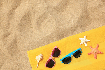 Beach accessories. Stylish sunglasses, yellow towel, starfishes and seashell on sand, top view. Space for text