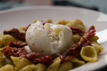Closeup of pesto conchiglie with sundried tomatoes and burrata cheese served in white plate