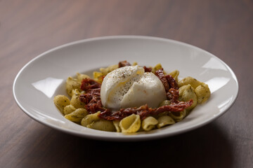 Pesto conchiglie with sundried tomatoes and burrata cheese served in white plate