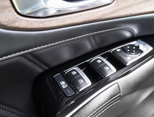 Door handle with power window control buttons of a luxury passenger car. Black perforated leather interior with stitching. Modern car black leather interior details.