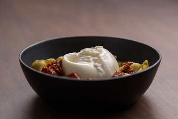 Pesto conchiglie with sundried tomatoes and burrata cheese served in black bowl