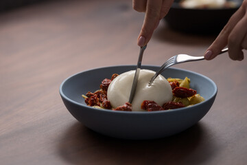 Closeup of pesto conchiglie with sundried tomatoes and cutting burrata cheese served in blue bowl
