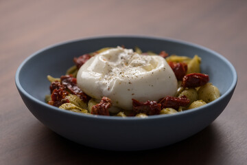 Pesto conchiglie with sundried tomatoes and burrata cheese served in blue bowl