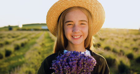 Beautiful little girl in hat on floral lavender field at summer day. Pretty child enjoying blooming...