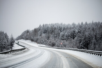 Photo of the winter road during the snowfall in Magadan, Russia. Snow showers on the trees and hills. Slush on the way. Fog and haze, low visibility due to snowstorm. Extreme weather conditions