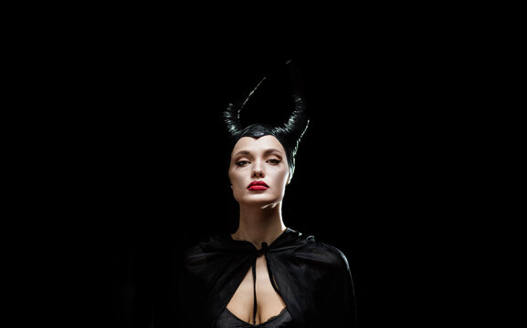 beautiful woman with devil witch horns in sorceress costume. Woman in Halloween costume posing against black background.