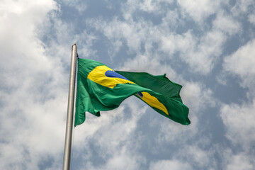 Uma Bandeira do Brasil tremulando ao vento em um dia com muitas nuvens no céu.