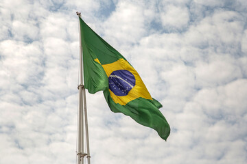 Uma Bandeira do Brasil tremulando ao vento em um dia com muitas nuvens no céu.