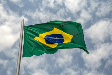 Uma Bandeira do Brasil tremulando ao vento em um dia com muitas nuvens no céu.