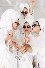 Young, beautiful women in bathrobes and glasses enjoying bachelorette party at spa or hotel and...