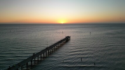 Aerial view of the pier and tranquil sea with a stunning sunset in the background.