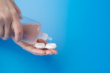 lens solution, female hands pouring cleaning liquid from a bottle into a contact lens case on a...