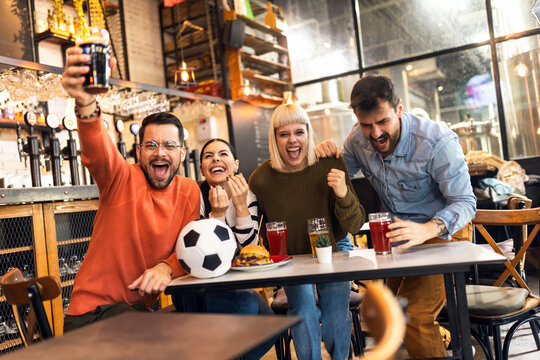 Excited soccer fans celebrating while watching soccer match on TV in bar.