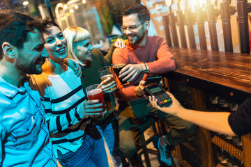 Diverse friends in bar paying with cellular device - obrazy, fototapety, plakaty