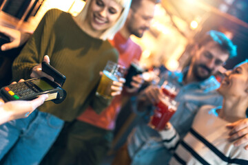 Diverse friends in bar paying with cellular device - obrazy, fototapety, plakaty