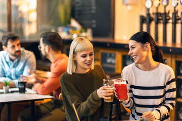 Smiling young friends drinking craft beer in pub