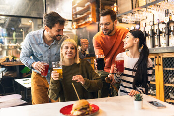 Smiling young friends drinking craft beer in pub