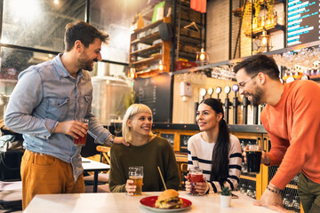 Smiling young friends drinking craft beer in pub