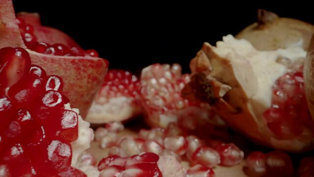 Two types of pomegranate, red and white seeds, they are split and scattered on the table. Dolly slider extreme close-up.